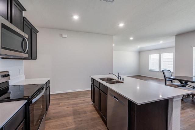 kitchen featuring sink, dark brown cabinets, dark hardwood / wood-style flooring, stainless steel appliances, and a center island with sink