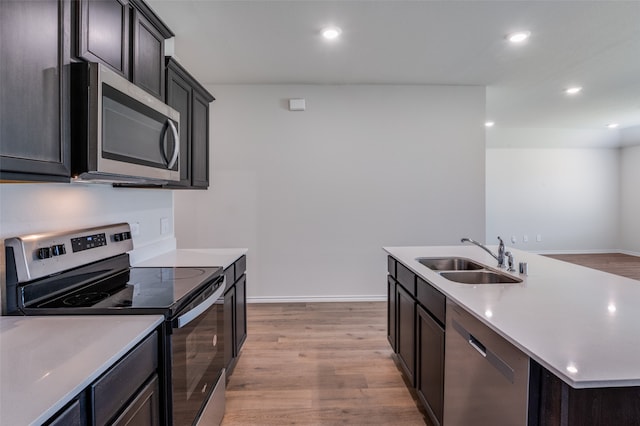 kitchen with appliances with stainless steel finishes, sink, light hardwood / wood-style floors, dark brown cabinetry, and a kitchen island with sink