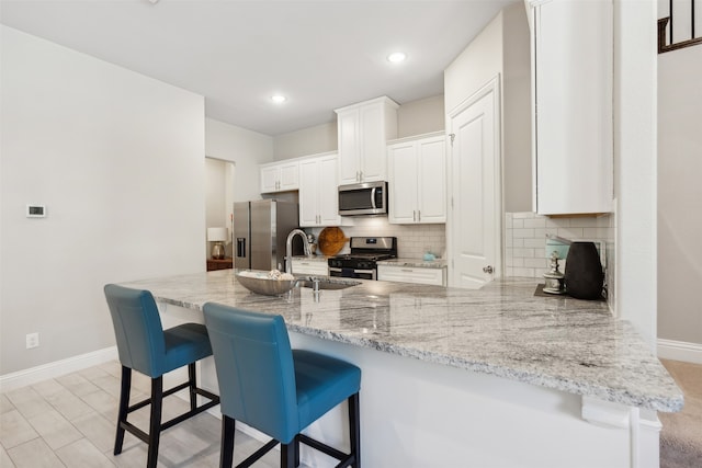 kitchen featuring kitchen peninsula, sink, light stone countertops, white cabinets, and appliances with stainless steel finishes