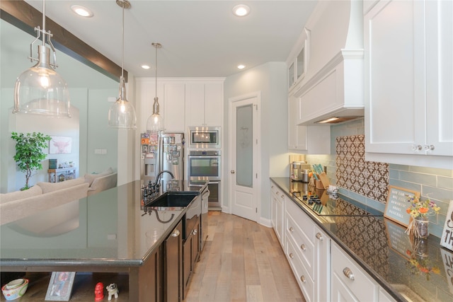 kitchen featuring light hardwood / wood-style flooring, stainless steel appliances, dark stone counters, decorative light fixtures, and white cabinetry