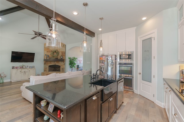 kitchen with white cabinets, light hardwood / wood-style flooring, beamed ceiling, a stone fireplace, and sink