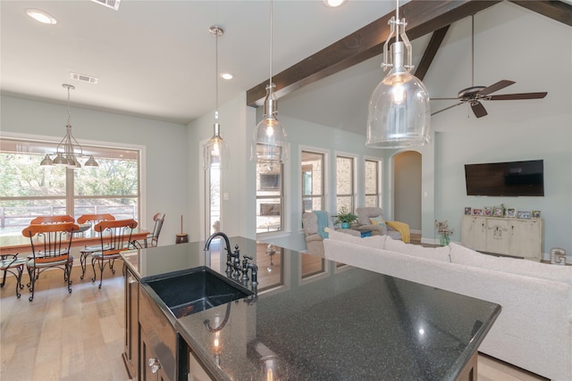 kitchen featuring a healthy amount of sunlight, dark stone counters, light wood-type flooring, and a center island with sink