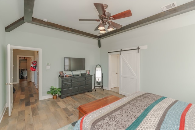 bedroom with washer / dryer, a barn door, ceiling fan, light hardwood / wood-style floors, and beam ceiling