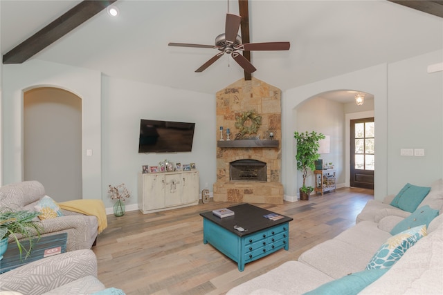 living room with ceiling fan, lofted ceiling with beams, light hardwood / wood-style flooring, and a stone fireplace