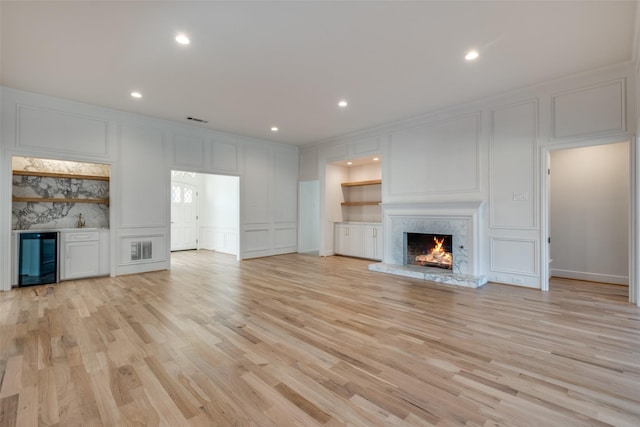 unfurnished living room with indoor bar, a high end fireplace, beverage cooler, and light hardwood / wood-style flooring