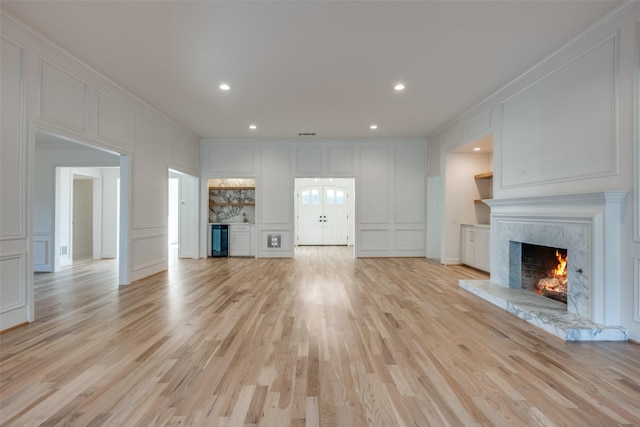 unfurnished living room with wine cooler, french doors, crown molding, light hardwood / wood-style flooring, and a high end fireplace