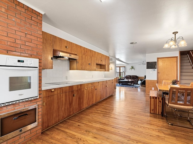 kitchen with black electric stovetop, light wood-type flooring, white oven, pendant lighting, and custom range hood