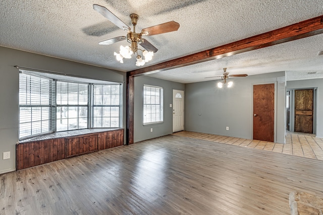 empty room with beam ceiling, a textured ceiling, light hardwood / wood-style flooring, and ceiling fan