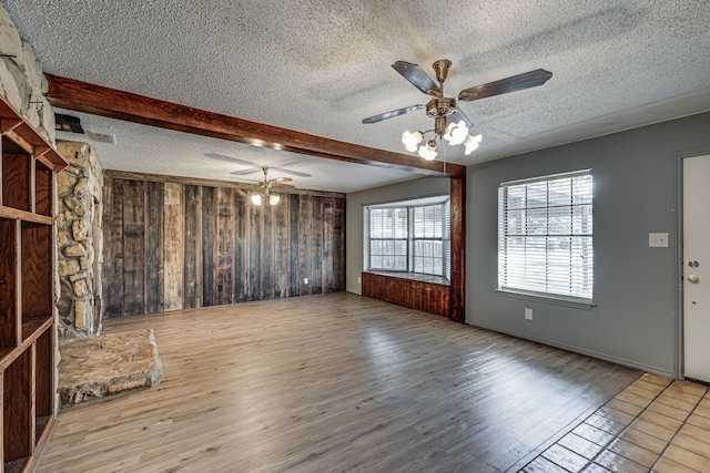 unfurnished living room featuring beamed ceiling, light wood-type flooring, a textured ceiling, and wooden walls