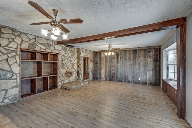 unfurnished living room featuring light wood-type flooring, a textured ceiling, ceiling fan, beam ceiling, and wood walls