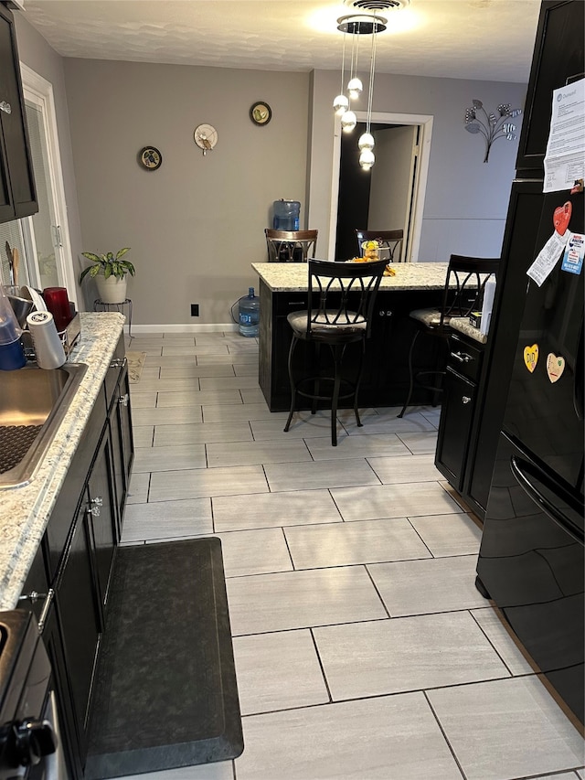 kitchen featuring black fridge, sink, light stone countertops, pendant lighting, and range