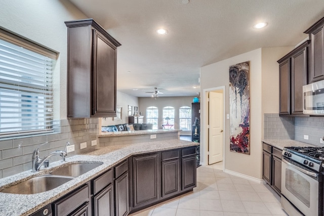 kitchen with light stone countertops, appliances with stainless steel finishes, sink, dark brown cabinets, and decorative backsplash