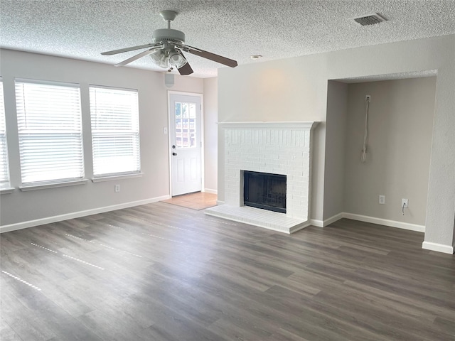 unfurnished living room with ceiling fan, a brick fireplace, dark hardwood / wood-style floors, and a textured ceiling