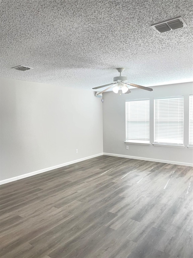 spare room with ceiling fan, dark wood-type flooring, a wealth of natural light, and a textured ceiling