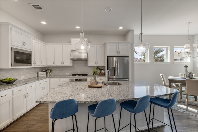 kitchen featuring dark hardwood / wood-style floors, an island with sink, stainless steel appliances, pendant lighting, and white cabinets