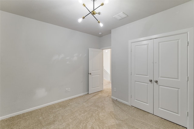 unfurnished bedroom with a closet, light colored carpet, and a notable chandelier