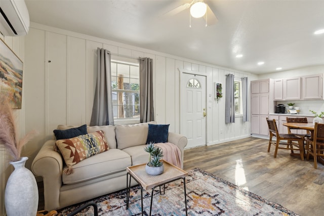 living room featuring light wood-type flooring, a wall mounted AC, ceiling fan, and a healthy amount of sunlight