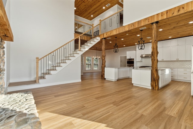 unfurnished living room with high vaulted ceiling, light wood-type flooring, a chandelier, and wooden ceiling