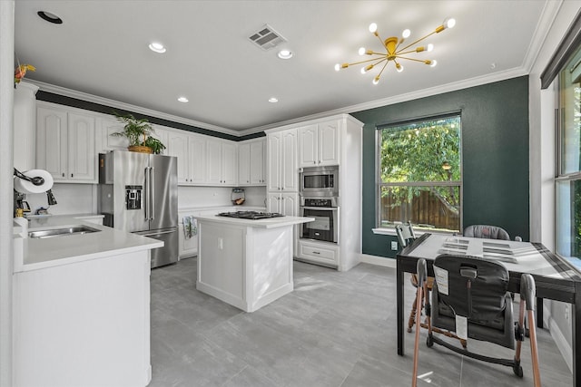 kitchen featuring appliances with stainless steel finishes, white cabinetry, a center island, crown molding, and an inviting chandelier