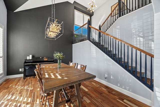 dining space with hardwood / wood-style flooring, a towering ceiling, and an inviting chandelier