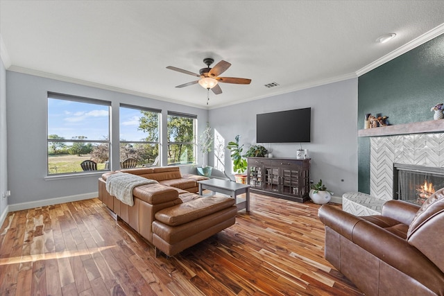 living room with hardwood / wood-style flooring, ceiling fan, ornamental molding, and a fireplace