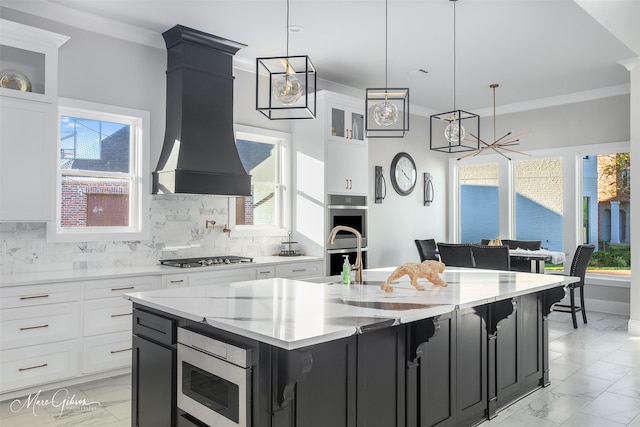 kitchen featuring pendant lighting, custom exhaust hood, an island with sink, and white cabinets