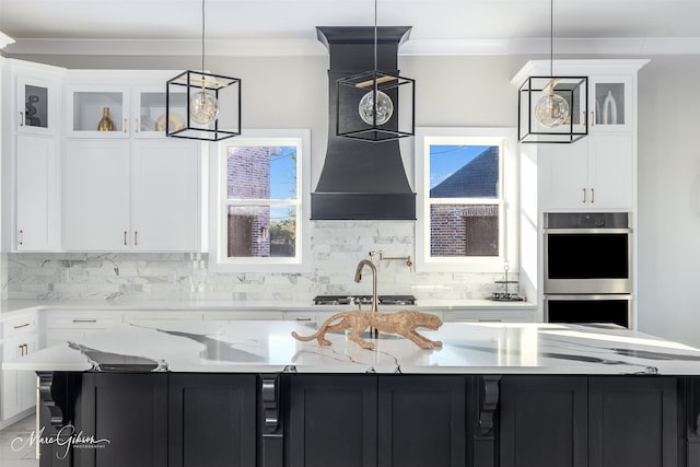 kitchen featuring hanging light fixtures, backsplash, a large island with sink, white cabinetry, and light stone counters