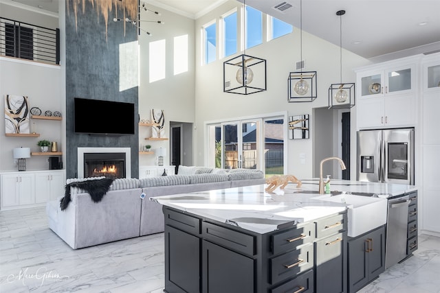 kitchen with stainless steel appliances, a towering ceiling, a fireplace, and white cabinets