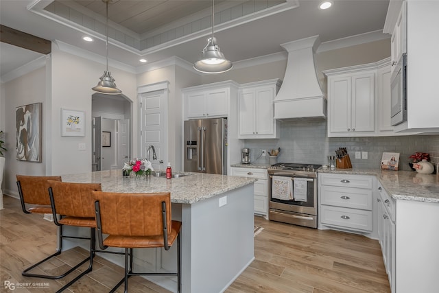 kitchen featuring a center island with sink, premium range hood, white cabinetry, light hardwood / wood-style floors, and stainless steel appliances