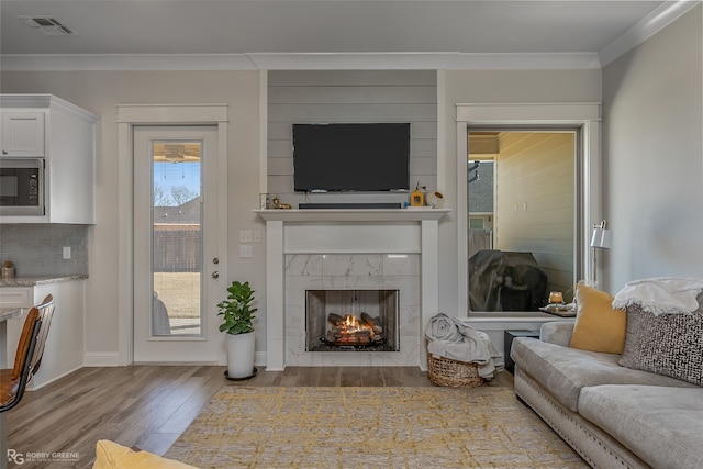 living room featuring a tiled fireplace, light hardwood / wood-style floors, and ornamental molding