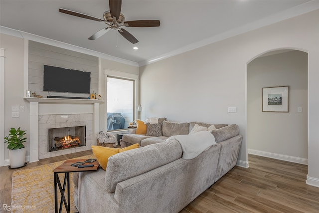 living room featuring crown molding, a tiled fireplace, wood-type flooring, and ceiling fan