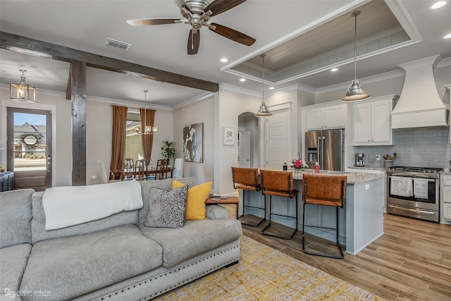 living room with light hardwood / wood-style flooring, ornamental molding, ceiling fan, and a raised ceiling