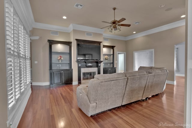 living room with crown molding, a tiled fireplace, wood-type flooring, and ceiling fan