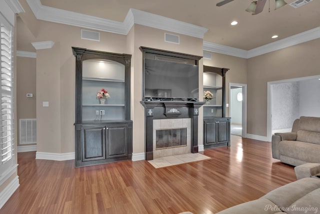 living room featuring ornamental molding, wood-type flooring, a tile fireplace, and ceiling fan