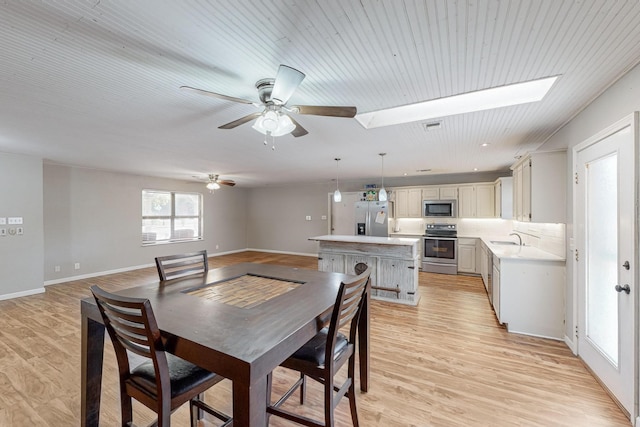 dining space featuring sink, ceiling fan, light wood-type flooring, and a skylight