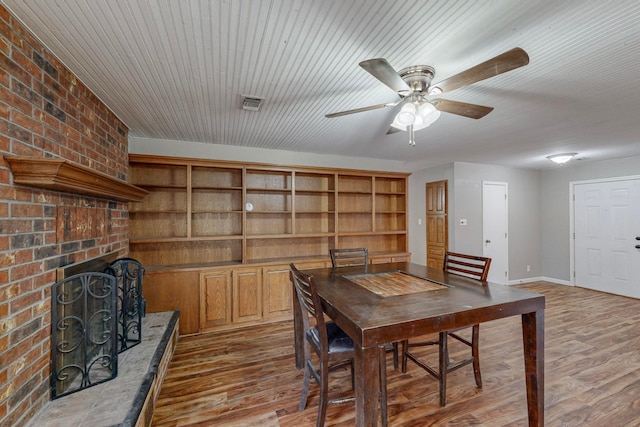 dining area with light hardwood / wood-style floors, brick wall, and a brick fireplace