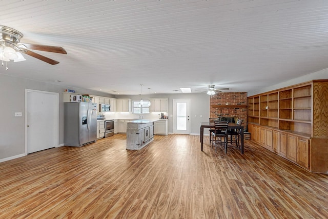 kitchen with appliances with stainless steel finishes, a fireplace, a kitchen island, light hardwood / wood-style floors, and pendant lighting