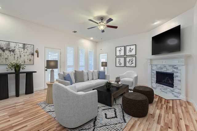 living room with light hardwood / wood-style floors, a stone fireplace, and ceiling fan