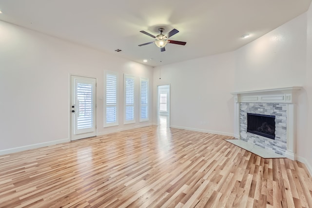 unfurnished living room with ceiling fan, a stone fireplace, and light hardwood / wood-style flooring