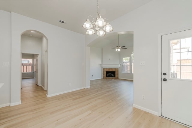 unfurnished living room with light hardwood / wood-style floors, lofted ceiling, a tile fireplace, and ceiling fan with notable chandelier