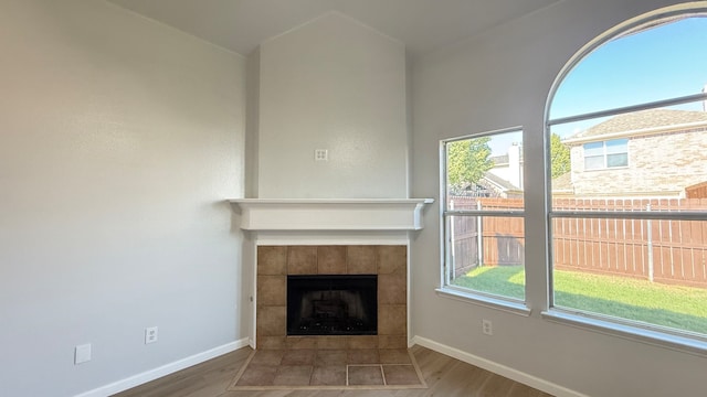 unfurnished living room with a healthy amount of sunlight, wood-type flooring, and a tile fireplace