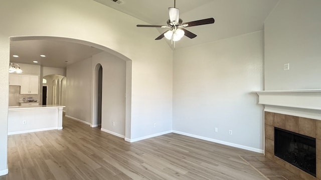 unfurnished living room featuring a tiled fireplace, vaulted ceiling, light hardwood / wood-style floors, and ceiling fan