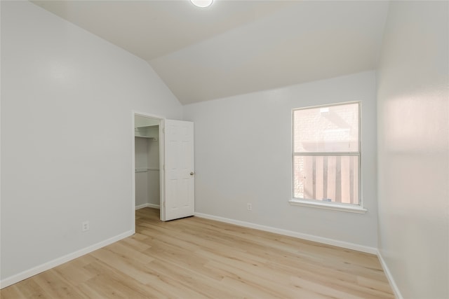 unfurnished bedroom with a closet, light hardwood / wood-style floors, vaulted ceiling, and a walk in closet