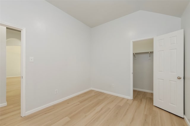 unfurnished bedroom featuring a spacious closet, lofted ceiling, a closet, and light hardwood / wood-style floors