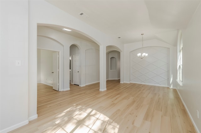 spare room with a notable chandelier and light wood-type flooring