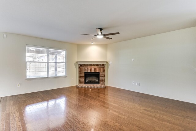 unfurnished living room with a ceiling fan, a brick fireplace, wood finished floors, and baseboards