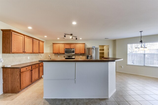 kitchen with brown cabinets, dark countertops, a center island, stainless steel appliances, and decorative backsplash