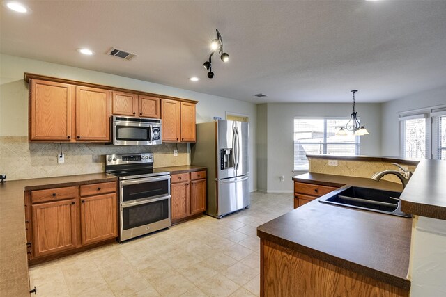 kitchen featuring visible vents, decorative backsplash, brown cabinetry, stainless steel appliances, and a sink