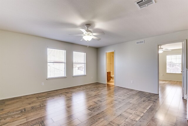 unfurnished room with a ceiling fan, wood finished floors, visible vents, and baseboards