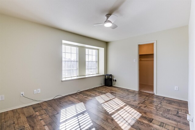 unfurnished bedroom featuring ceiling fan, a walk in closet, baseboards, and wood finished floors